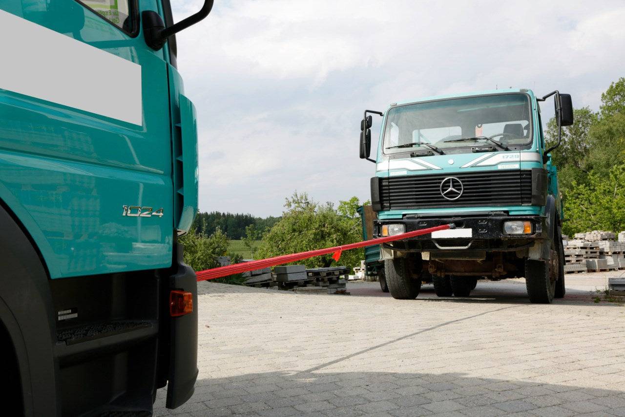 Abschleppschlinge für LKW, Traktoren, Baumaschinen etc. bis 56 Tonnen verbindet zwei LKWs bei einer Pannenhilfe auf einem Industriegelände.