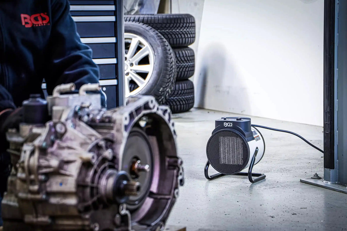 Heizlüfter elektrisch 3 kW von BGS in Autowerkstatt neben Reifen und Getriebe. Effiziente Wärmequelle für kalte Arbeitsbereiche.