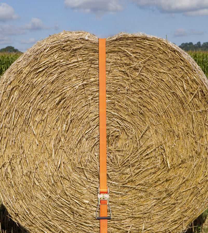 Ratschenzurrgurt mit Spitzhaken 2-teilig 2000 kg orange sichert eine große Rundballen-Heurolle auf dem Feld, UV-beständig nach DIN EN 12195-2.